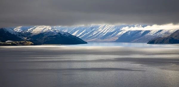 New Zealand, Otago, Lake Hawea. The Southern Alps revealed through a small gap between dense snow clouds and the surface of