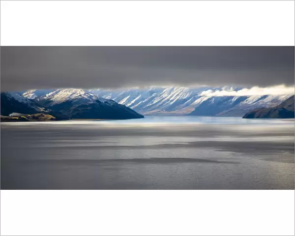 New Zealand, Otago, Lake Hawea. The Southern Alps revealed through a small gap between dense snow clouds and the surface of