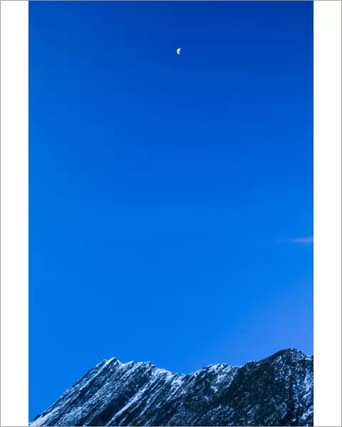 New Zealand, Otago, Mt Aspiring National Park. Half moon over an ice covered peak in the National Park