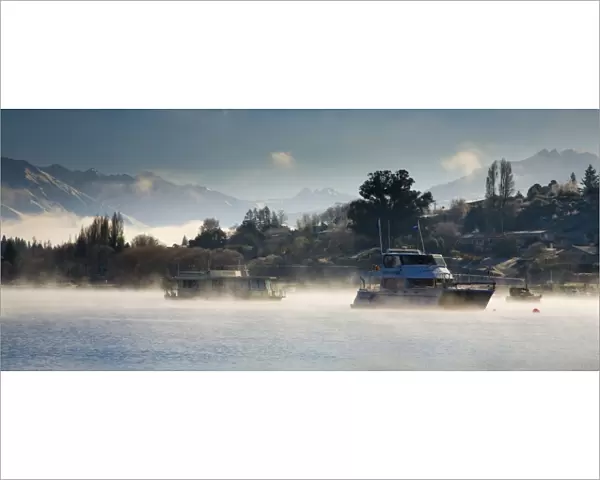 New Zealand, Otago, Lake Wanaka. Boats moored on Lake Wanaka engulfed by rising mist on a cold