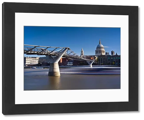 England, London, St Pauls Cathedral. A boat passes below the London Millennium Bridge which links the south bank of the Thames with St Pauls Cathedral and