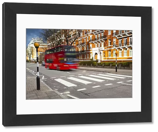 England, London, Abbey Road. A red London bus approaches the famous pedestrian crossing at Abbey Road, made famous by the cover of the Beatles album of the