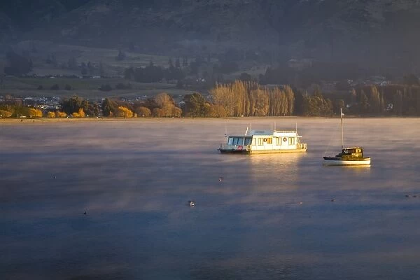 New Zealand, Otago, Lake Wanaka. The warm hues of sunset highlight the rising mist engulfing boats anchored on