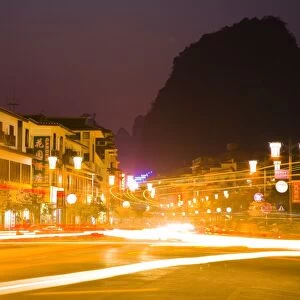 China, Guangxi Zhuang Autonomous Region, Yangshuo City. Busy traffic running through a chinese city at night with a backdop of limestone