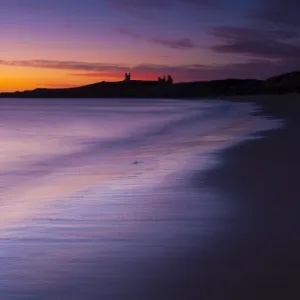 England, Northumberland, Embleton Bay. A colourful display of pre-dawn colours relected upon the wet sands of Embleton Bay, overlooked by the dramatic ruins of